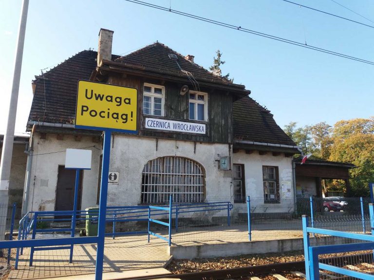 Widok dworca od strony torów. Żółty znak ostrzegawczy "Uwaga pociąg!".