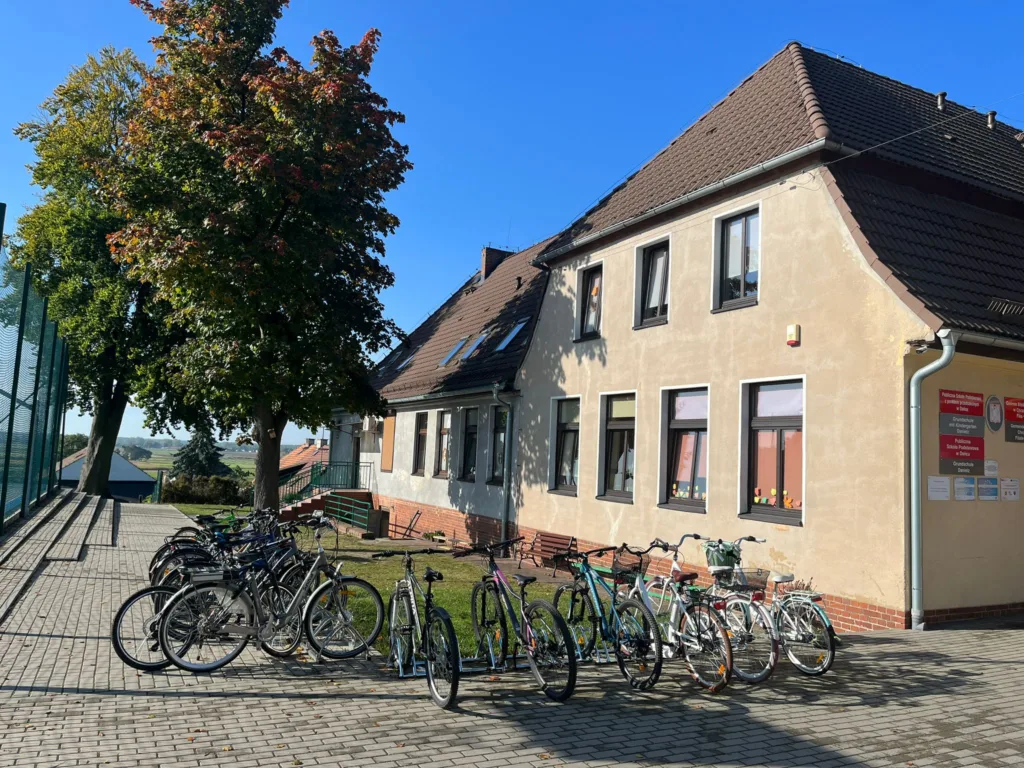Budynek szkoły. Przed wejściem kilkanaście zaparkowanych rowerów.