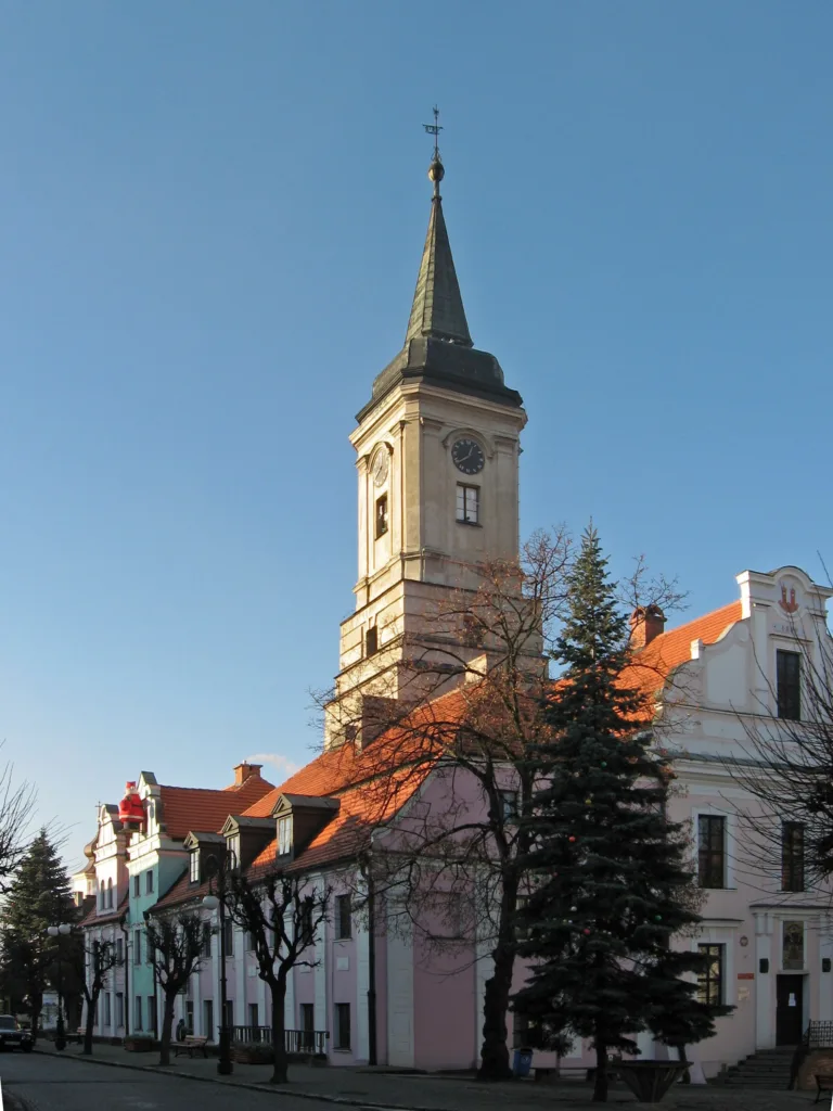 Zabytkowy budynek z wysoką wieżą. Na niższych częściach dachu pomarańczowa dachówka.