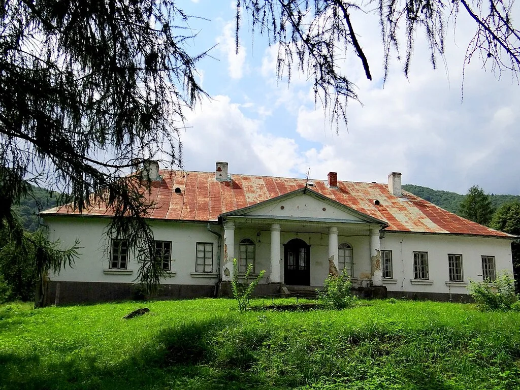 Widok dworu od frontu w otoczeniu zieleni.