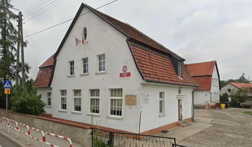 Widok budynku szkoły od strony ulicy. Biała elewacja, pomarańczowa dachówka.